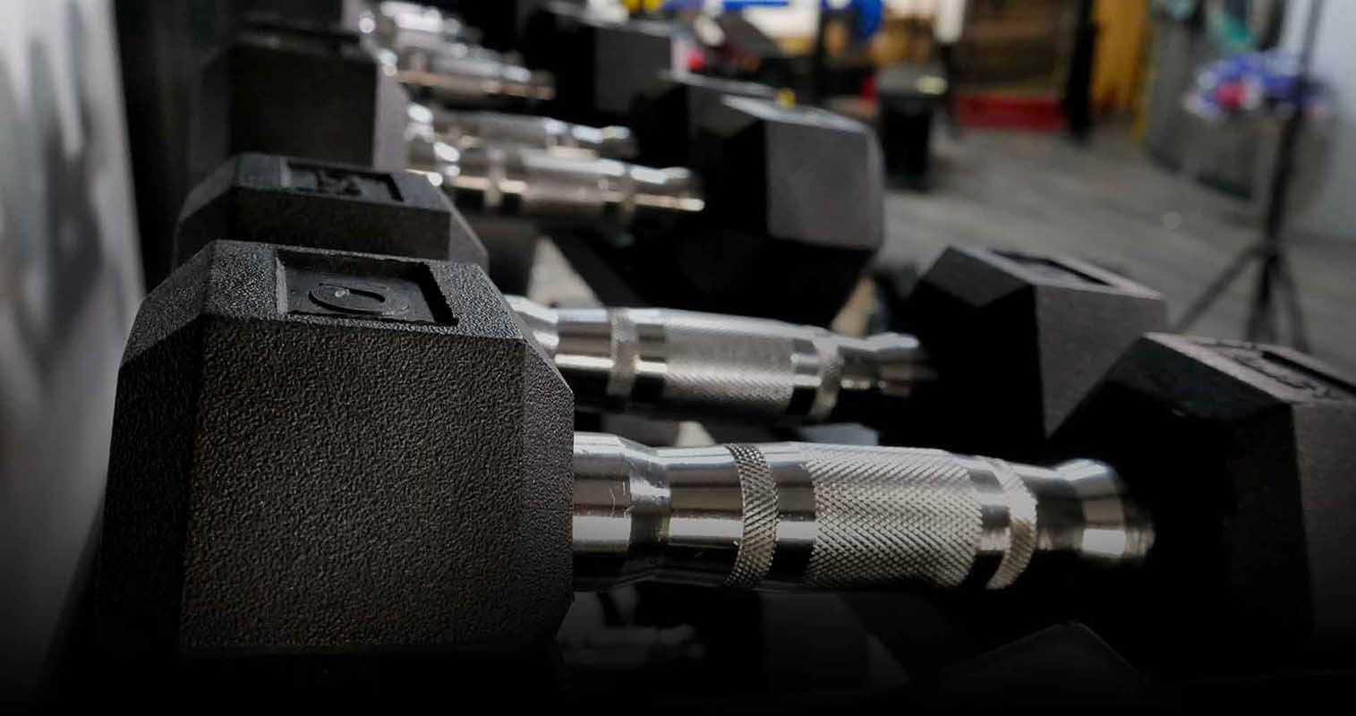 Hexagonal dumbbells of different weight levels in a line on a dumbbell stand.