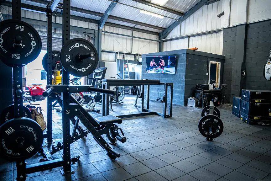 a weight bench, half rack, barbell, weight plates and prone row bench in a gym setting