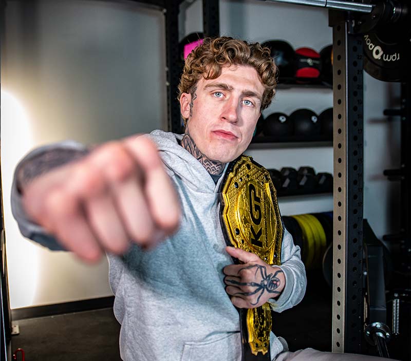 Ciarain Shanahan punches with his fist while holding a fighting belt